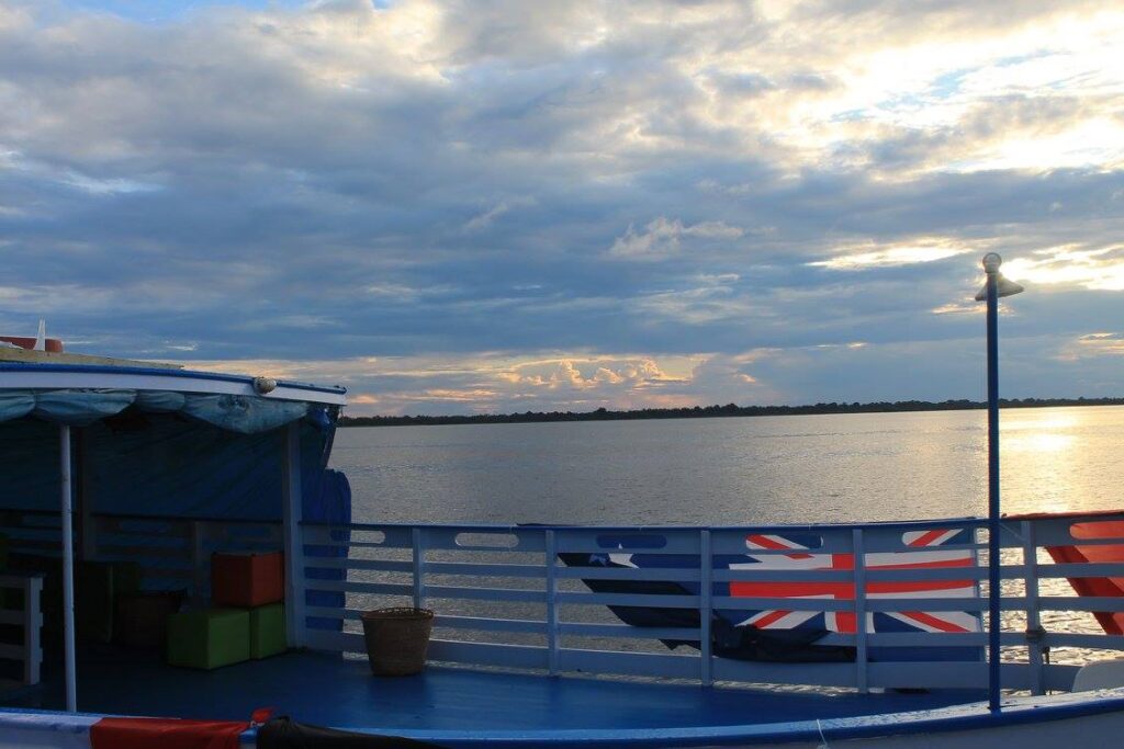 Udsigt over den spejlblanke flod i Amazonas fra rækværket på en båd ved skumringstid
