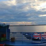 Udsigt over den spejlblanke flod i Amazonas fra rækværket på en båd ved skumringstid